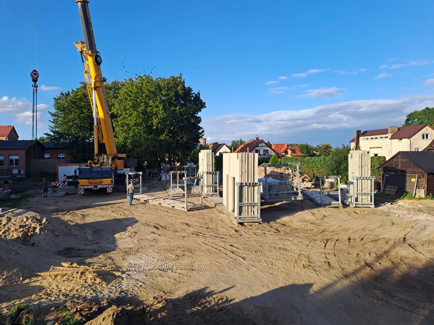 Prefabrykowane ściany w stojakach transportowych na placu budowy w Człuchowie, obok żuraw